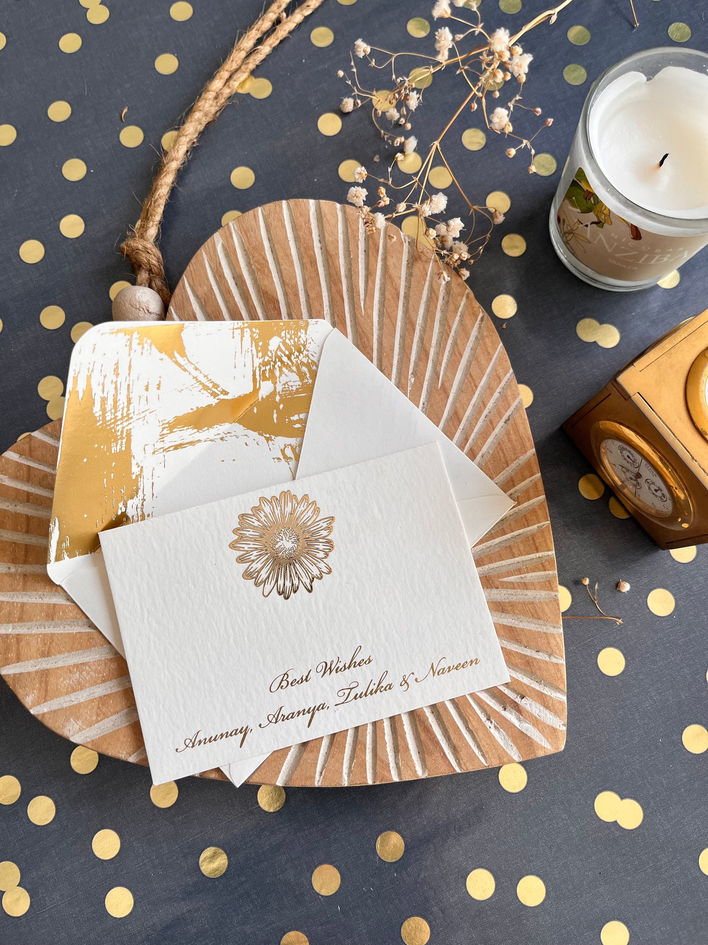 A flat card with a gold embossed daisy motif and matching lettering, displayed on a dotted background with a decorative element on the side.