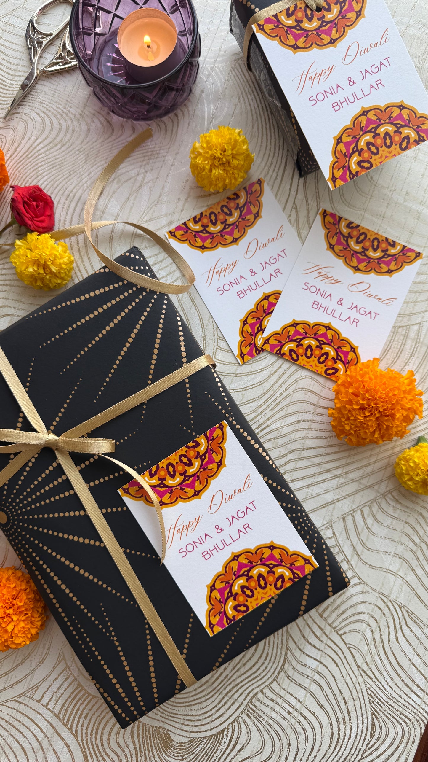 Gift box with decorative label on a textured surface with marigold flowers and candles.