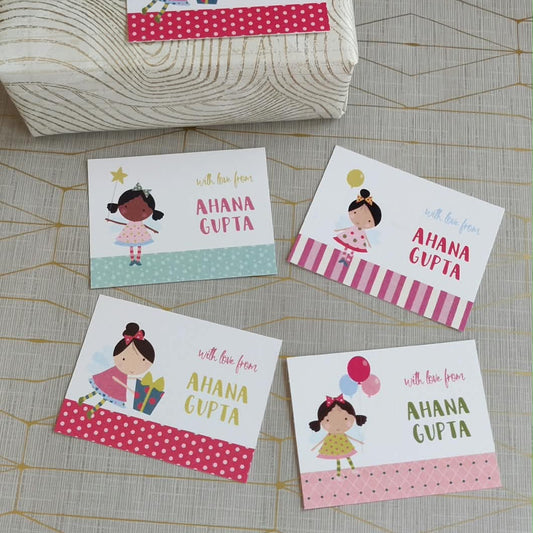 Five personalized greeting cards with cartoon girl illustrations and the text 'with love from AHANA GUPTA' are arranged on a light beige patterned surface, with one card placed on top of a wrapped gift box.
