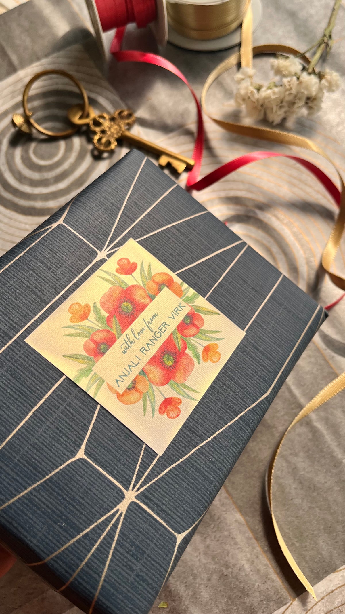 A navy blue gift box with a personalised gift label featuring red poppies