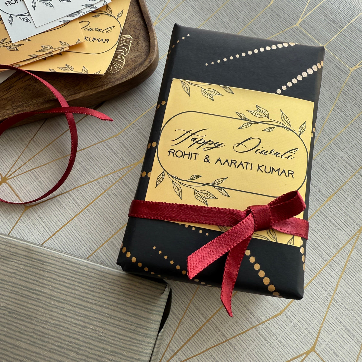 Gift box with personalized 'Happy Diwali' label and red ribbon on a textured surface.