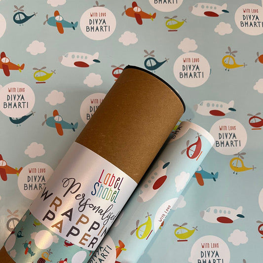A roll of wrapping paper placed on a light blue patterned background with cartoon planes helicopters and clouds