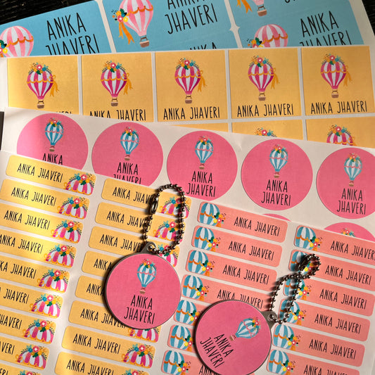 A sheet of round pink stickers with the text 'ANKA JHAVERI' and a hot air balloon illustration, alongside rectangular pink and yellow labels, shown on a white background.