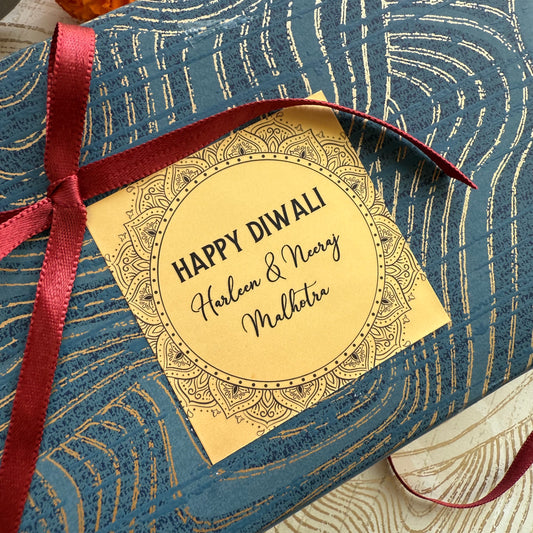 Gift box with a 'Happy Diwali' tag and red ribbon on a blue patterned background