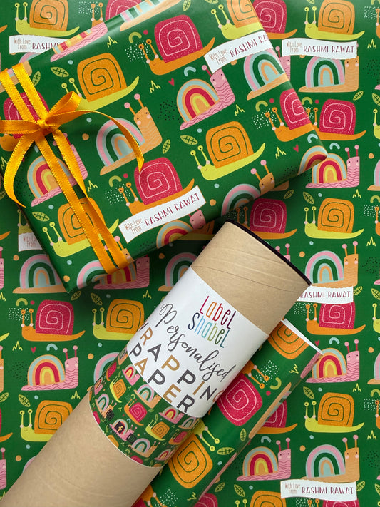 A roll of wrapping paper and a wrapped gift box with a matching patterned wrap, featuring a colorful retro snail design on a green background. The gift is tied with a yellow ribbon,