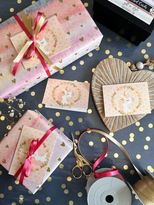 Unicorn and flowers themed gift tags on Gift-wrapped items with ribbons on a dark surface with gold polka dots