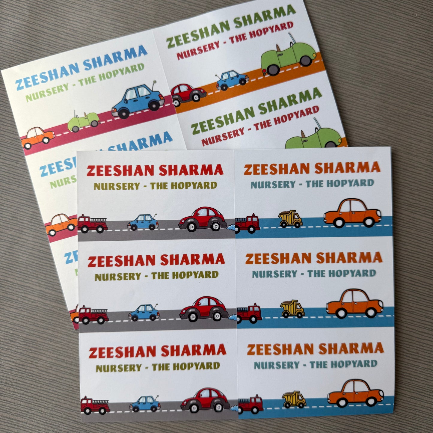 A set of custom printed stickers for a garden or nursery, featuring the text 'ZEESHAN SHARMA NURSERY - THE HOPYARD' and colorful cartoon cars on a road, arranged on a gray textured surface.