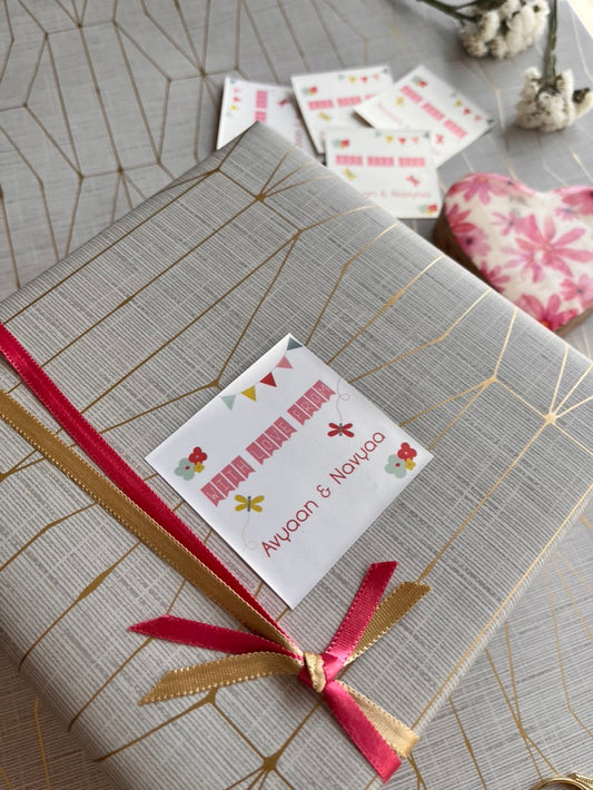 A wrapped gift box with a textured gray and gold patterned paper, tied with a pink and gold ribbon, and adorned with a custom printed gift label