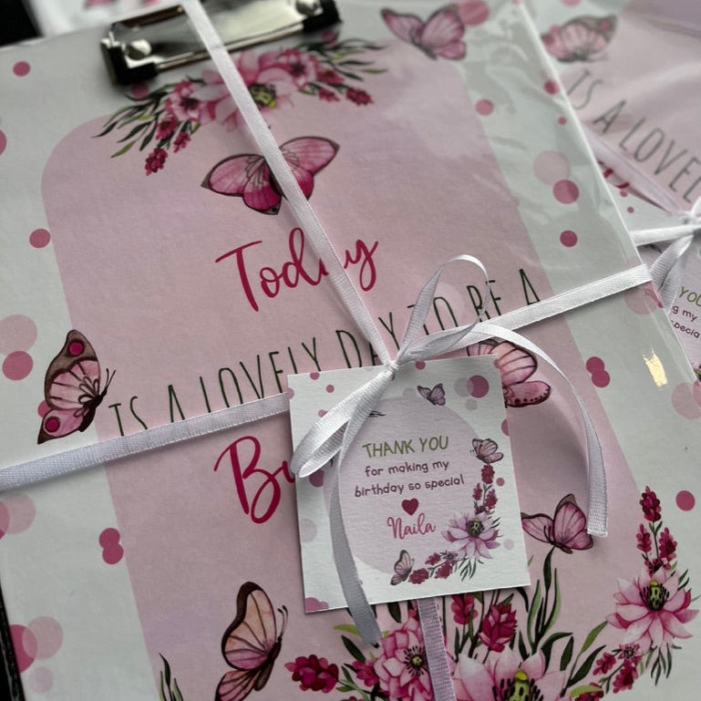 a clipboard with a beautiful pink butterfly design with a white ribbon and a thank you card as a return gift present for birthdays