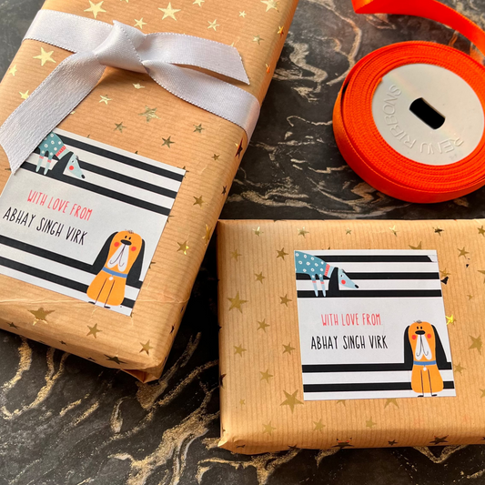 Two wrapped gift boxes on a dark marble surface, wrapped in tan paper with gold stars, a white ribbon, and a black-and-white striped label