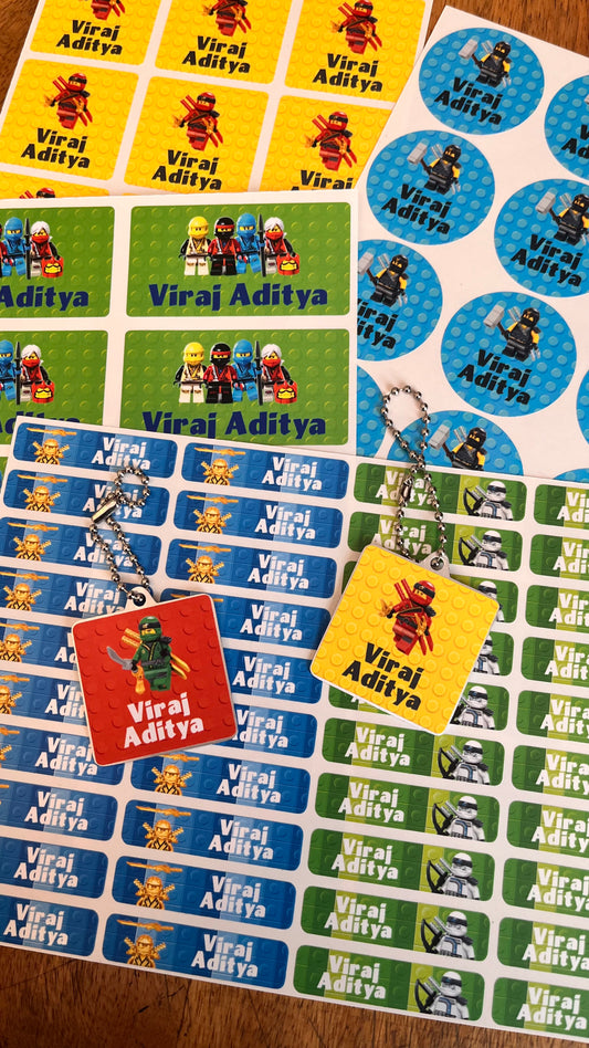 Custom printed sticker sheets and keychains featuring Lego minifigures and the name 'Viraj Aditya' on a wooden surface.
