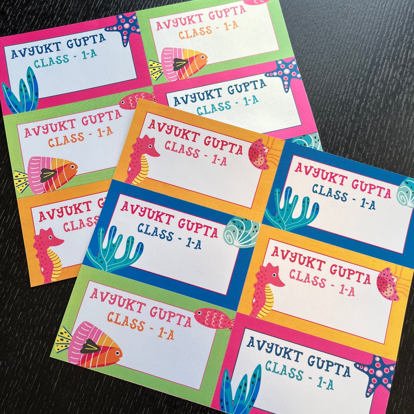 colorful underwater-themed name tags arranged on a dark textured surface. Each tag has a white center with the text bright borders in pink, green, blue, yellow, and orange, decorated with seahorses, fish, and starfish illustrations.