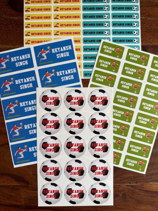 personalised, waterproof school name labels soccer player graphics, alongside sheets of round football themed stickers and a sheet of rectangular name stickers, all arranged on a dark wood background.