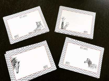 Four rectangular greeting cards arranged on a dark wooden surface. Each card has a gray and white chevron border, a white center, and a black-and-white animal illustration (tiger, giraffe, horse, zebra).