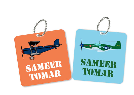 Two round metal bag tags with an airplane design and the name 'Samir' printed on them, one tag is orange and the other is blue.