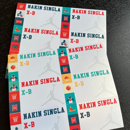 A stack of custom printed book labels featuring the  name and class in red and teal, with basketball-themed graphics and silhouettes of basketball players