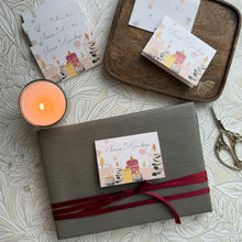 Gift box with a red ribbon and a card on a patterned surface with a candle.
