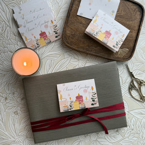 Gift box with a red ribbon and a card on a patterned surface with a candle.