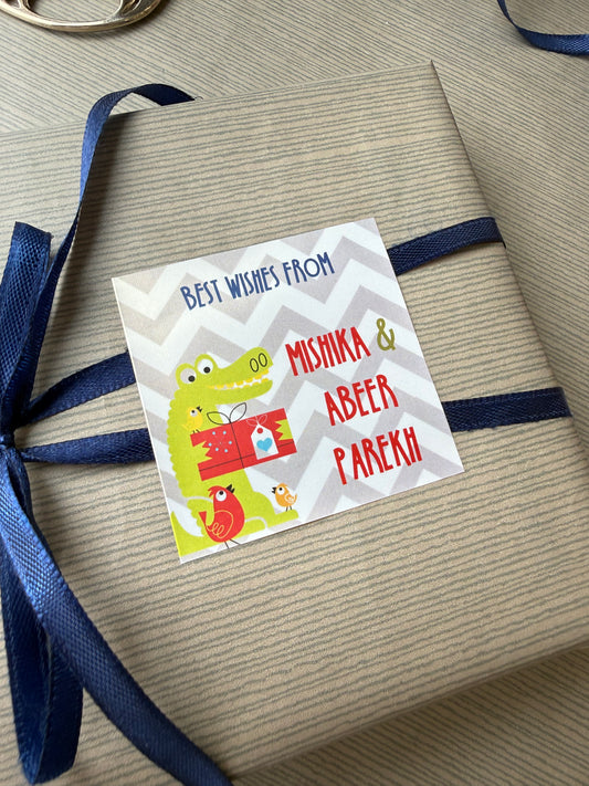 A personalized gift tag with cartoon crocodile and bird illustrations, wrapped around a kraft paper gift box tied with a navy blue ribbon.