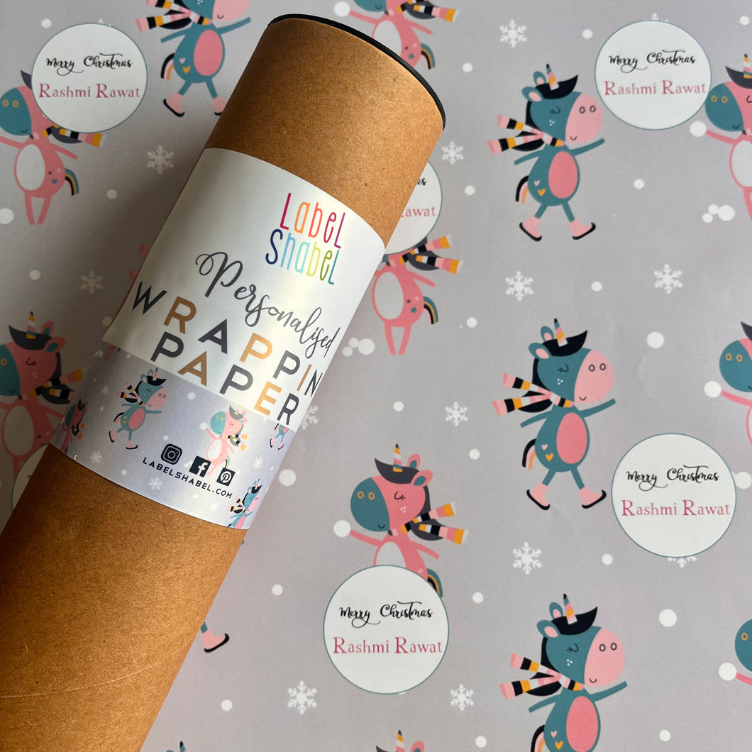 A roll of personalized wrapping paper with a dancing unicorn motif, placed on a background with various designs including snowflakes and cute creatures.