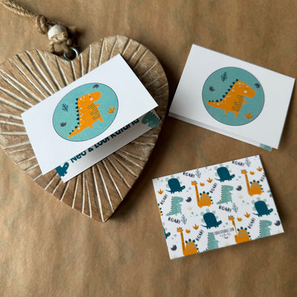 A set of children's birthday cards featuring cute dinosaur illustrations, styled on a brown kraft paper background with a wooden heart-shaped box.