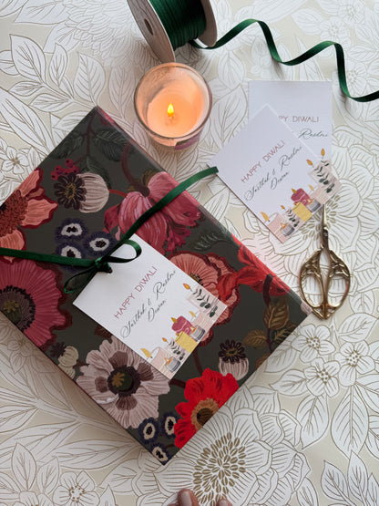 Floral-patterned gift box with a candle and decorative scissors on a floral tablecloth.