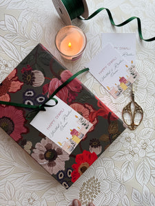 Floral-patterned gift box with a candle and decorative scissors on a floral tablecloth.