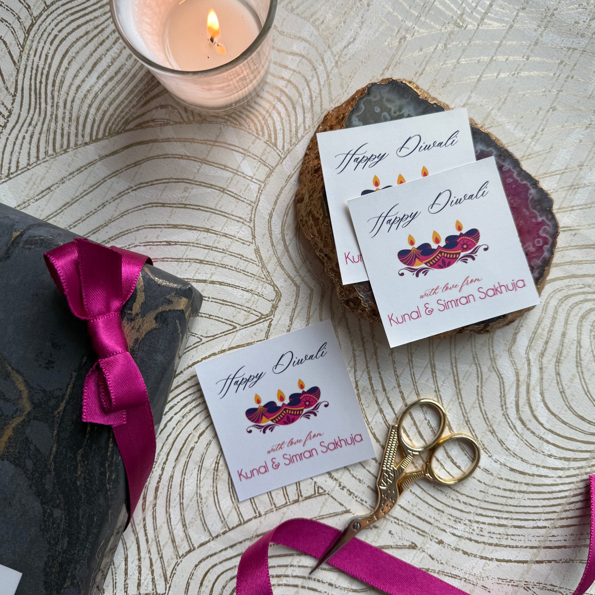 Happy Diwali cards with personalized names, a candle, and scissors on a textured surface.