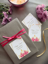 Gift box with pink ribbon and floral card on a wooden surface with flowers and candles.