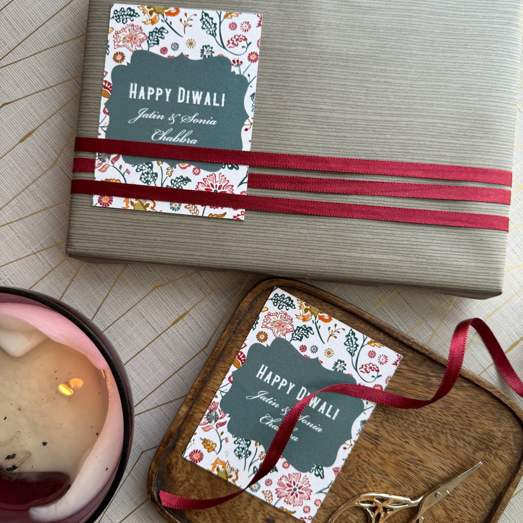 Gift wrapped in brown paper with red ribbon and 'Happy Diwali' card on wooden surface.