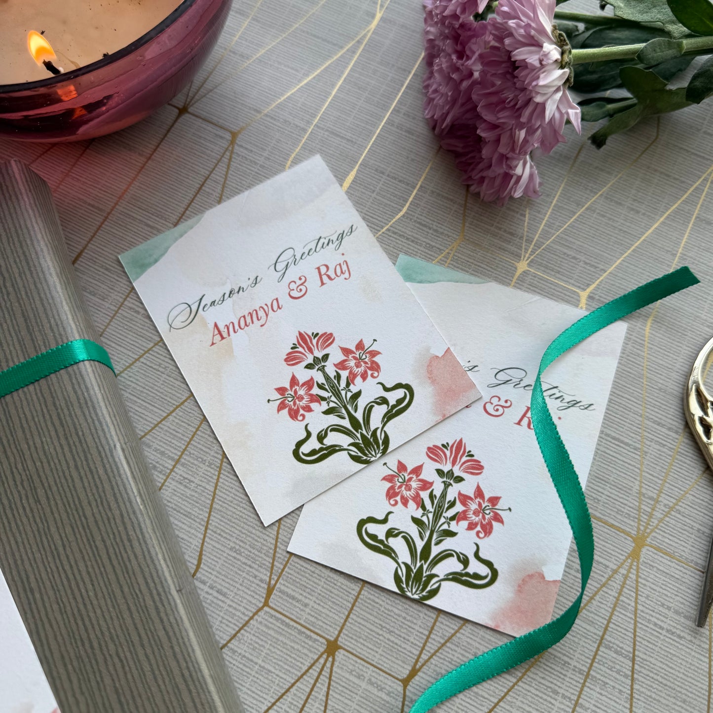 Two greeting cards with floral designs on a decorative surface with a candle and flowers.