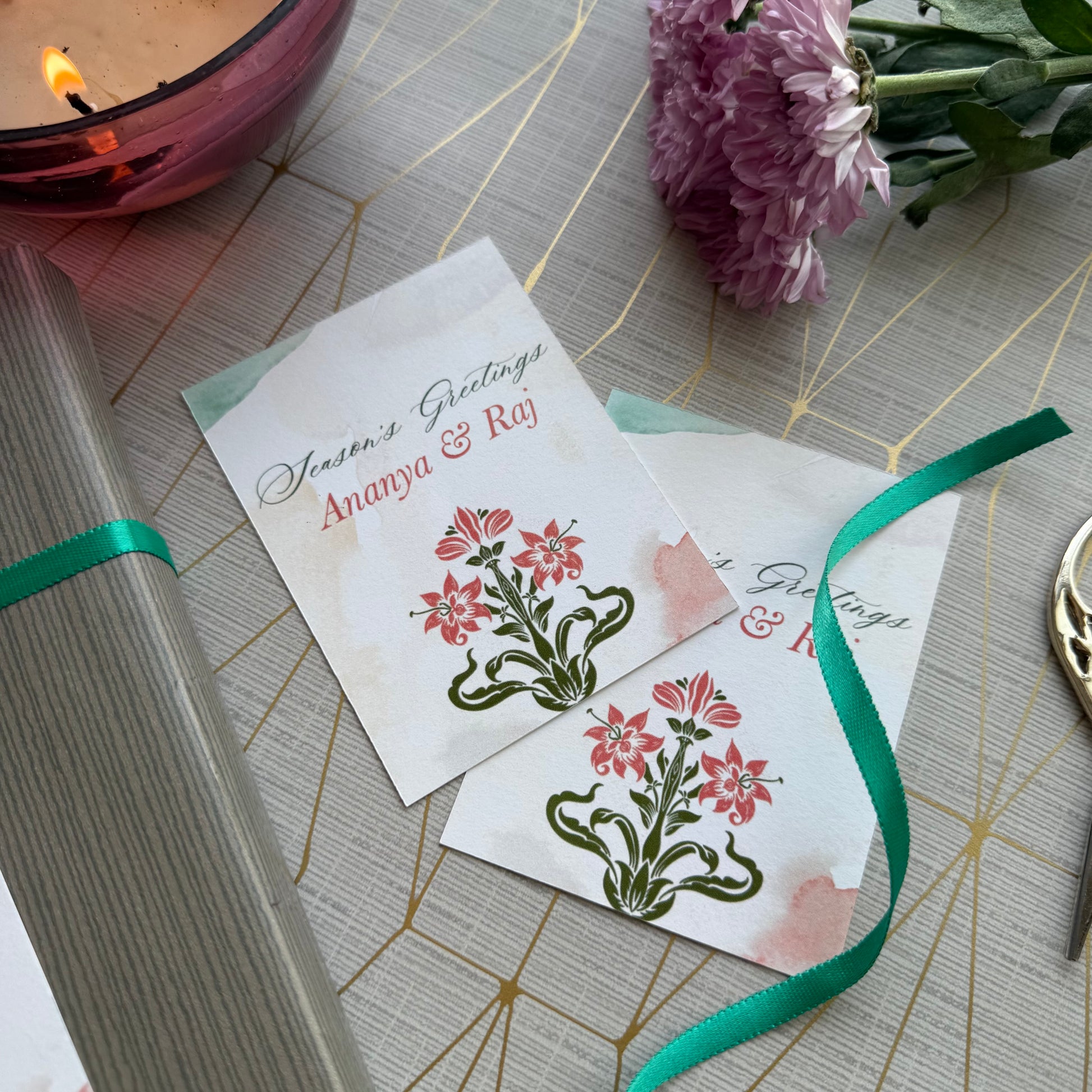 Two greeting cards with floral designs on a decorative surface with a candle and flowers.