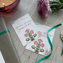 Two greeting cards with floral designs on a decorative surface with a candle and flowers.