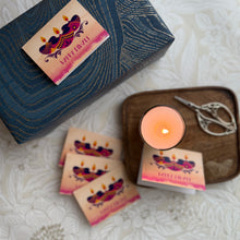 Candle with decorative packaging and a pair of scissors on a textured surface