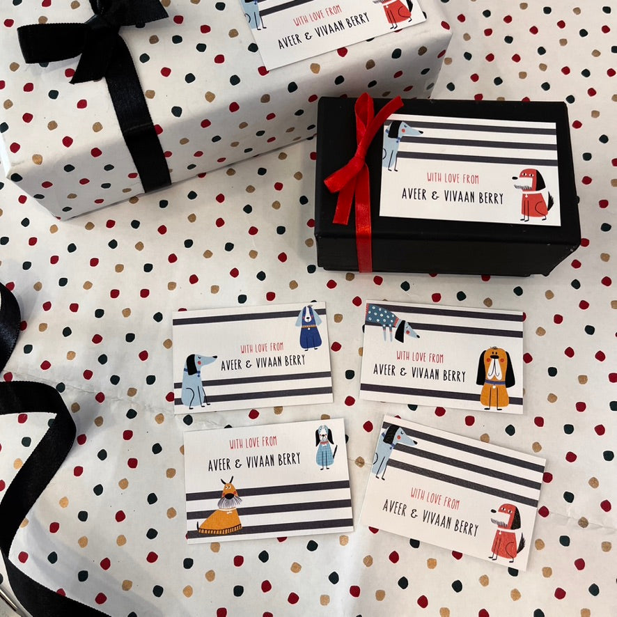 A styled flat-lay of gift packaging featuring white gift boxes and cards with black and red stripes, polka dots, and cartoon dog illustrations. The cards read 'WITH LOVE FROM AVIK & VIVAAN BIRKT'.