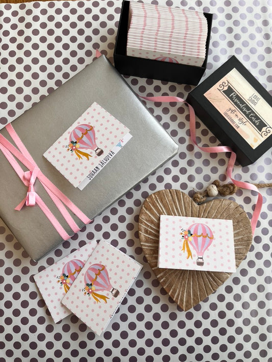 A styled flat-lay of gift-wrapping supplies and decorative paper products on a white backgroundfeautring a personalised gift tag with a hot air balloon illustration