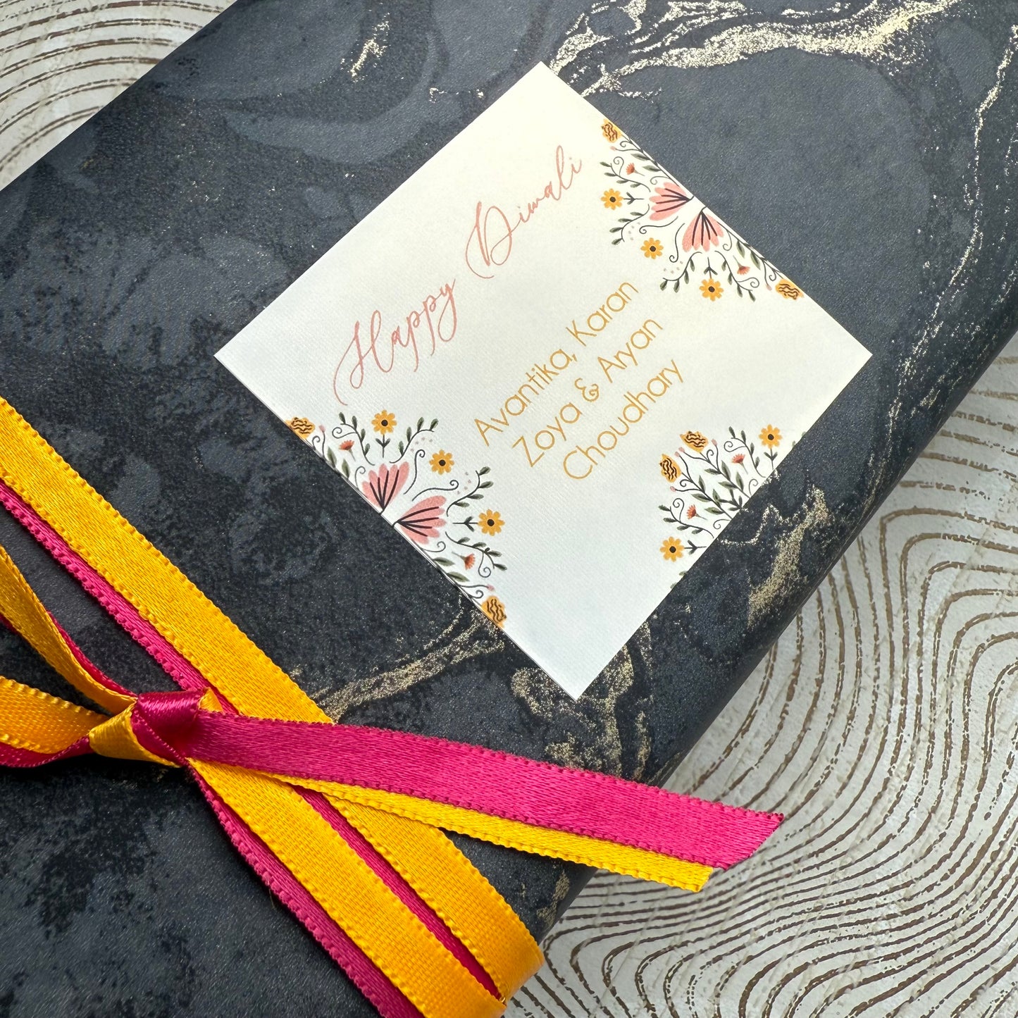 Gift box with a 'Happy Diwali' card tied with ribbons on a textured surface