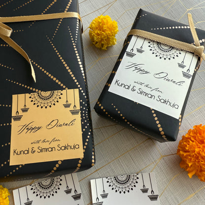 Two black gift boxes with Diwali-themed labels and marigold flowers on a patterned surface.