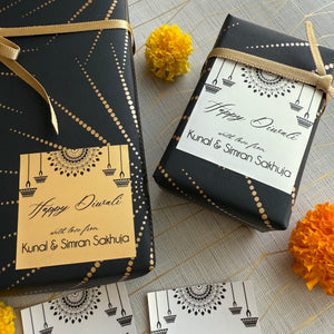 Two black gift boxes with Diwali-themed labels and marigold flowers on a patterned surface.