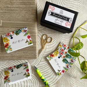 Folded gift tag in white background with tropical leaves and birds and best wishes sign with name inside on top of a gift