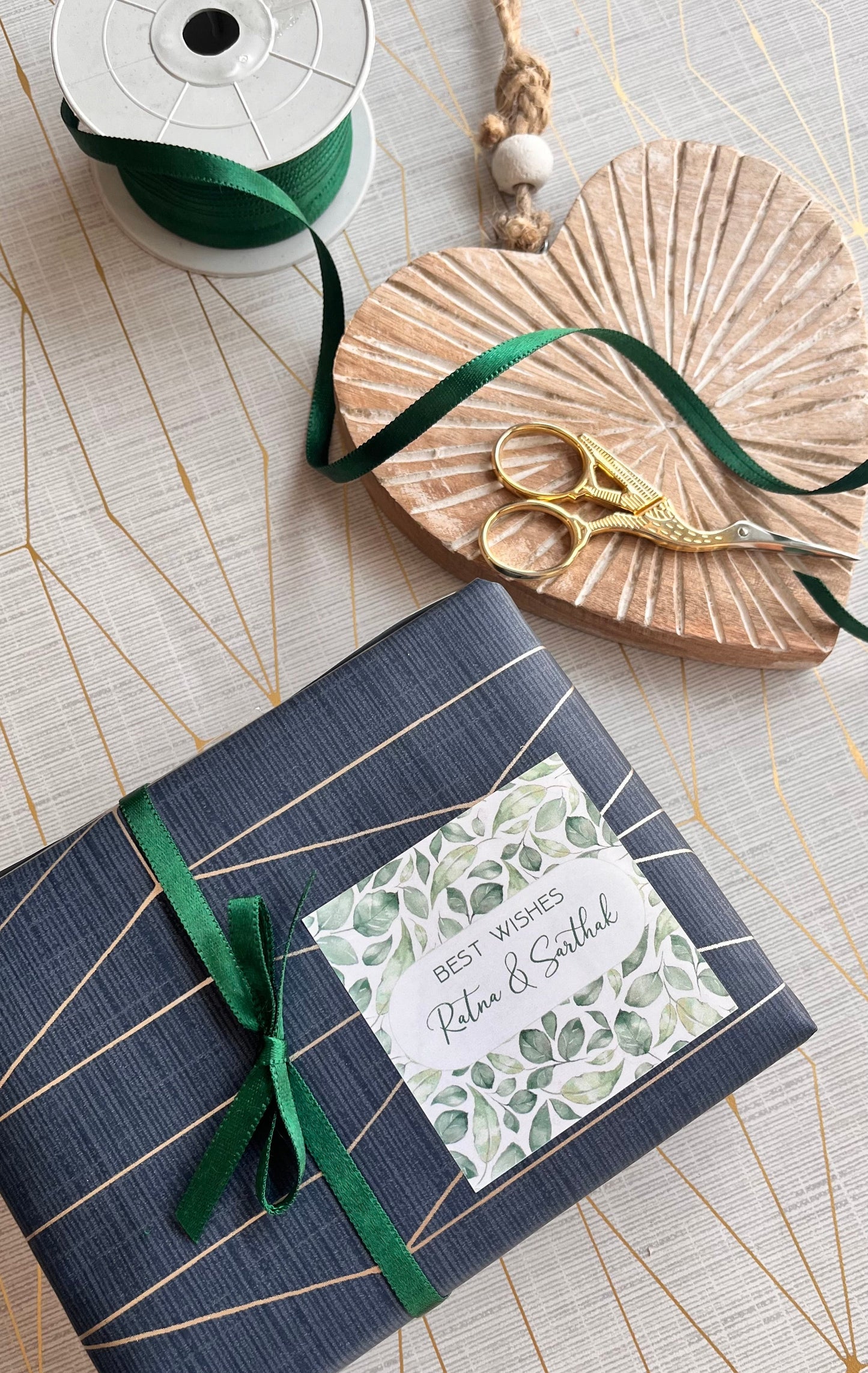 A wrapped gift box or book in dark navy blue wrapping paper with thin gold diagonal stripes, tied with a green ribbon and bow. A decorative paper label is attached on the front.