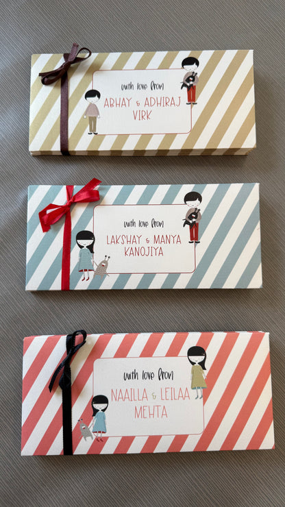 Three personalized rmoney envelopes with striped patterns and ribbon bows, arranged vertically on a gray textured surface. Each box has a white label with custom names and small cartoon illustrations of children.