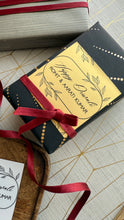 Black gift box with gold label and red ribbon on a textured surface