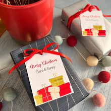 Personalized Christmas gift tags with 'Merry Christmas' text and decorative ribbon, attached to a gift wrapped in a blue paper with a red ribbon.