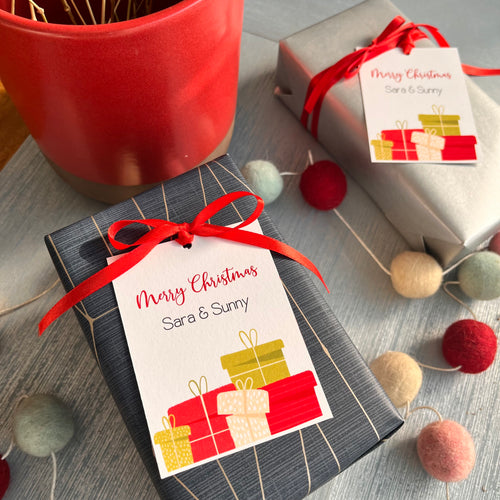 Personalized Christmas gift tags with 'Merry Christmas' text and decorative ribbon, attached to a gift wrapped in a blue paper with a red ribbon.