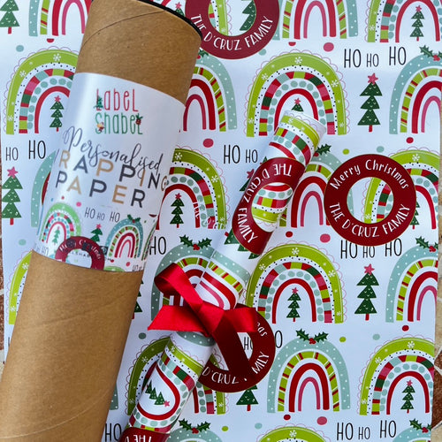 A roll of personalized wrapping paper with 'Ho Ho' text, Christmas trees and mistletoe patterns, and a red ribbon.