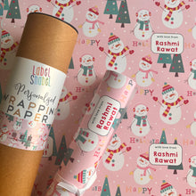 A roll of personalized wrapping paper with a holiday snowman theme, including Christmas trees and the text 'HAPPY'.