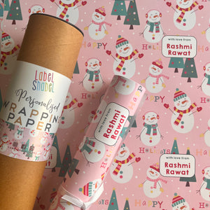 A roll of personalized wrapping paper with a holiday snowman theme, including Christmas trees and the text 'HAPPY'.