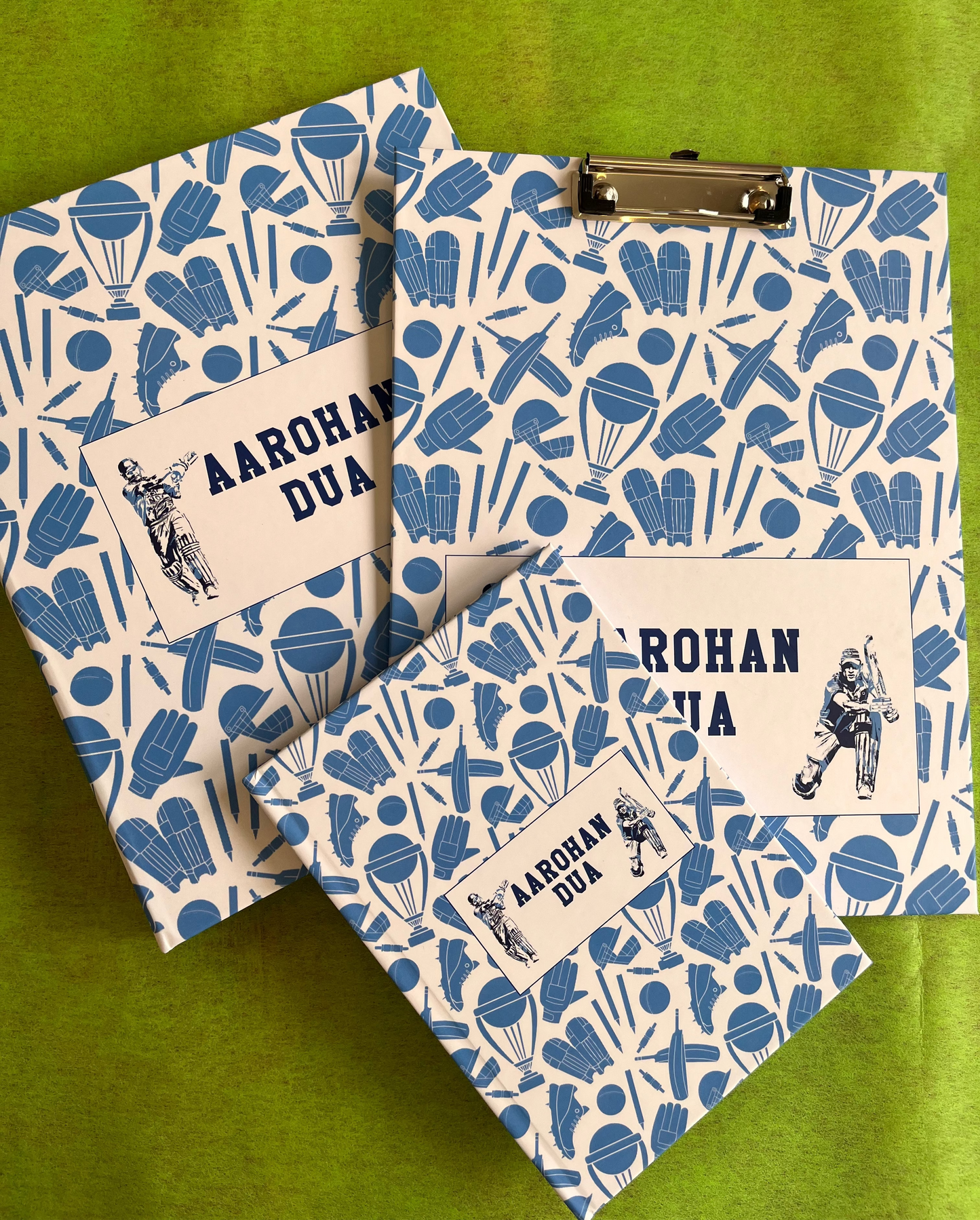 A set of school supplies with a blue and white design, including a notebook, clipboard, and a ring folder, all personalized with 'Aarohan DuA' written on the covers.