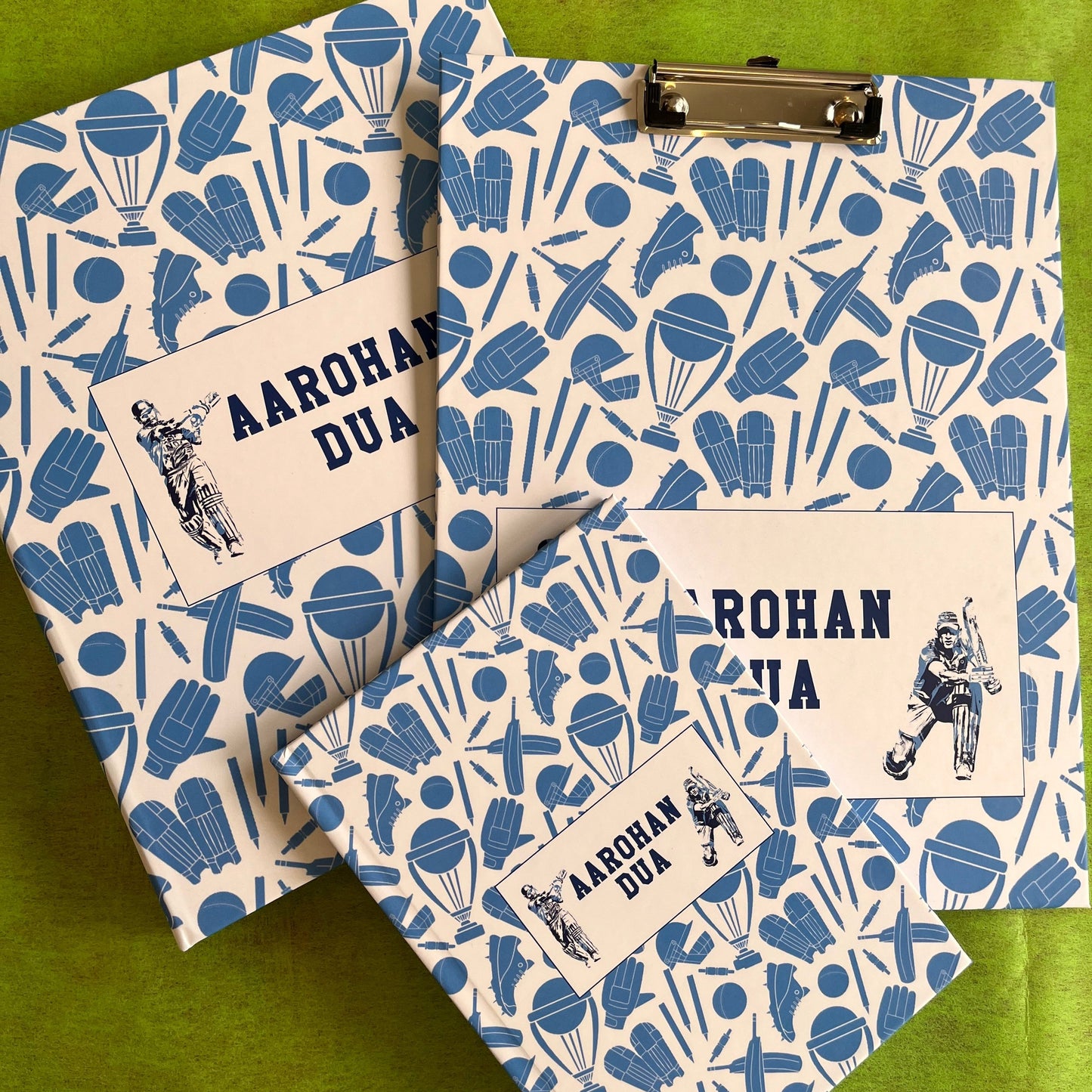A set of school supplies with a blue and white design, including a notebook, clipboard, and a ring folder, all personalized with 'Aarohan DuA' written on the covers.